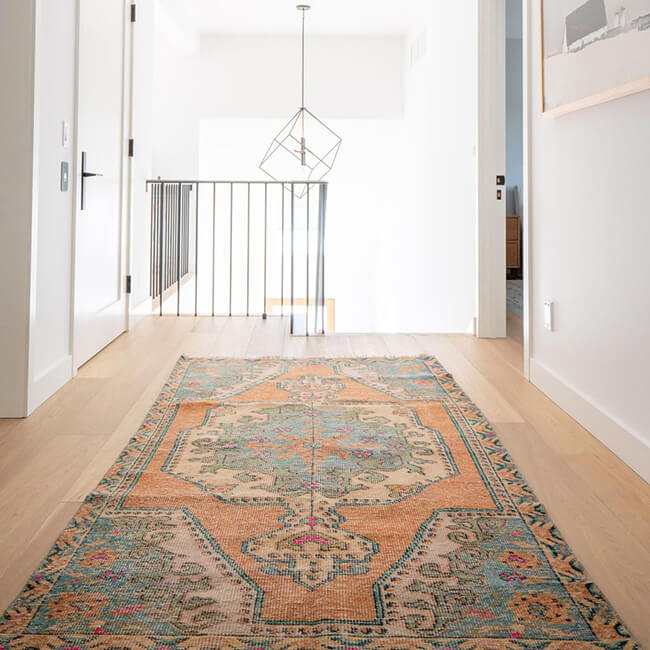 Patterned 5x7 rug placed in a bright hallway with light wood flooring and white walls