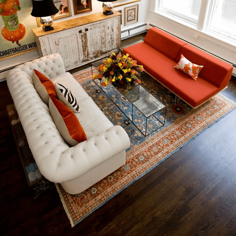 Traditional 8x12 rug beneath the seating area of a colorful living room with orange and white sofas