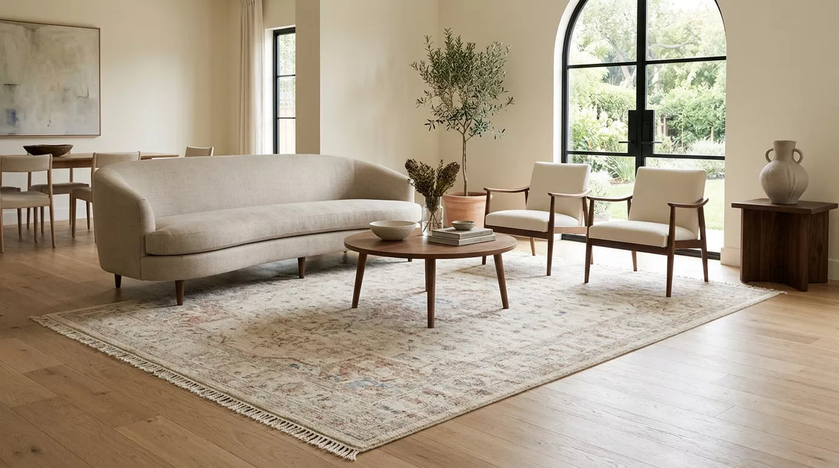 Handmade 8x12 rug anchoring an open-plan living room with a curved sofa, accent chairs, and bright natural light