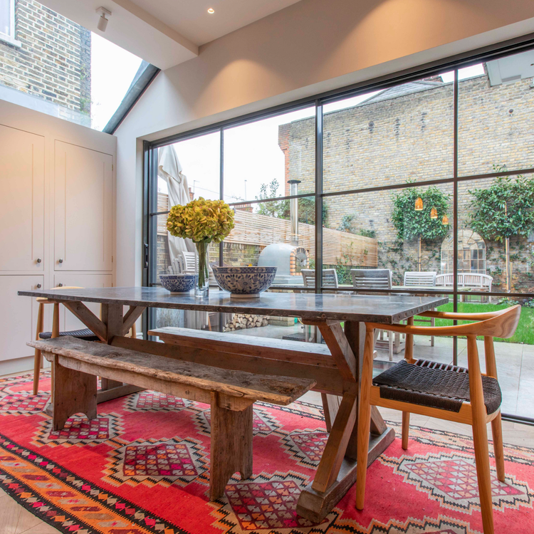 Handmade red kilim rug beneath a wooden dining table in a bright contemporary dining room