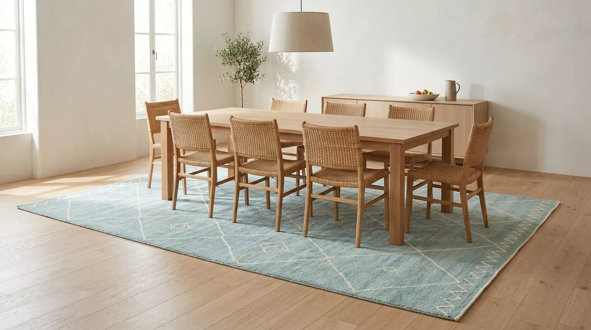 Pale blue Moroccan rug with an ivory diamond pattern and zigzag border under a wooden dining table with eight woven chairs