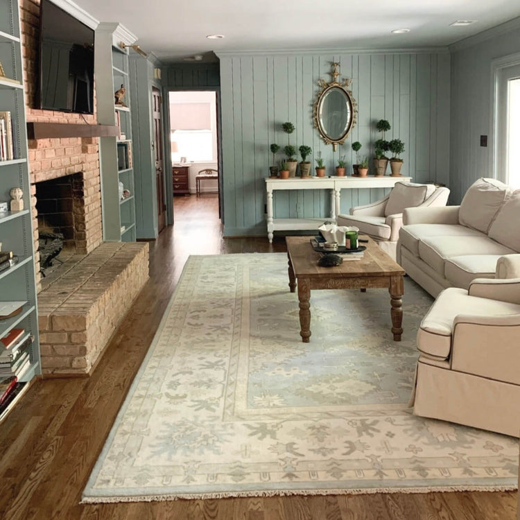 Handmade Oushak rug in a neutral living room with white seating and a stone fireplace