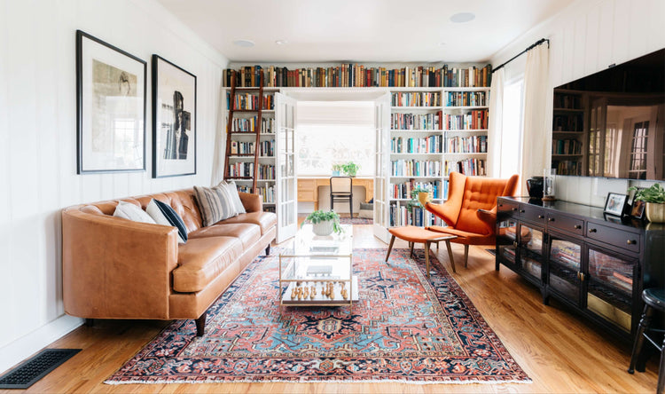 Handmade Persian rug in a bright home library living room with floor-to-ceiling bookshelves and leather seating