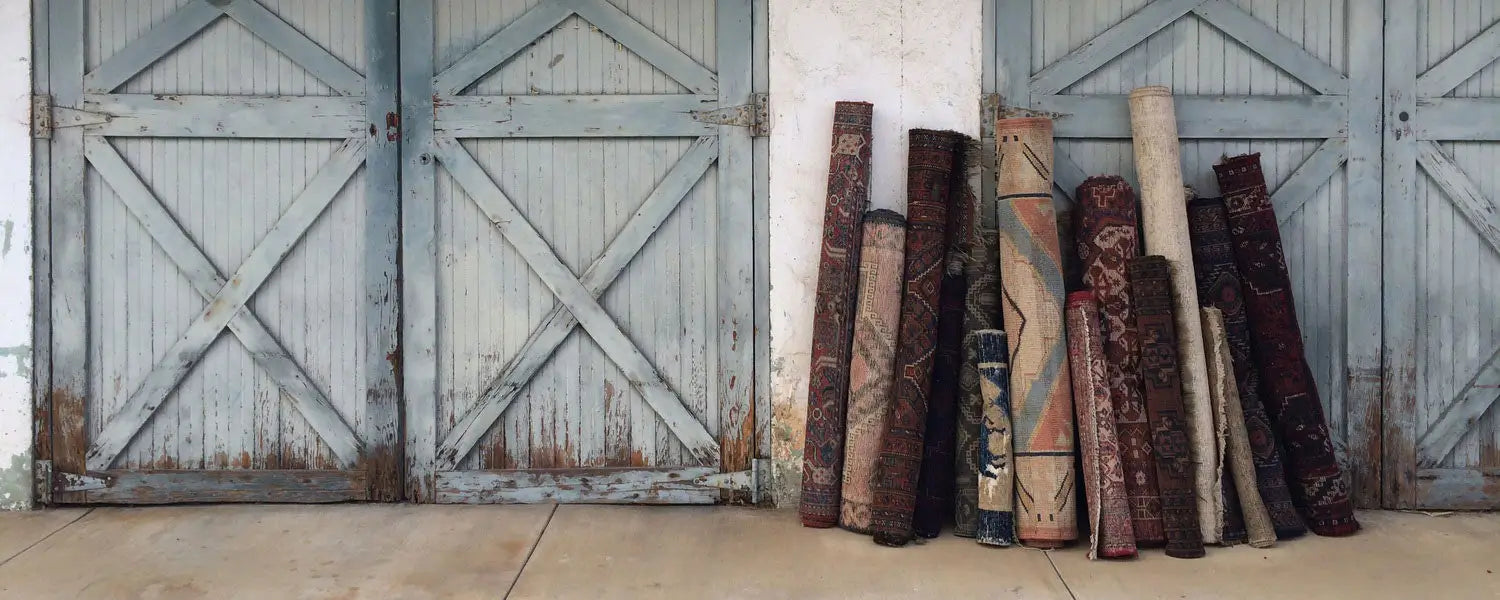 Collection of rolled vintage rugs displayed against rustic blue wooden doors