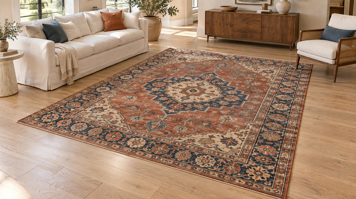 Vintage hand-knotted wool area rug with a terracotta field, indigo medallion and wide floral border, laid on a light oak floor in a living room with a cream sofa and walnut sideboard